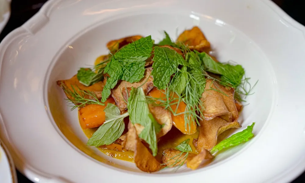 A gourmet dish with crispy vegetables and fresh herbs served in a white bowl.