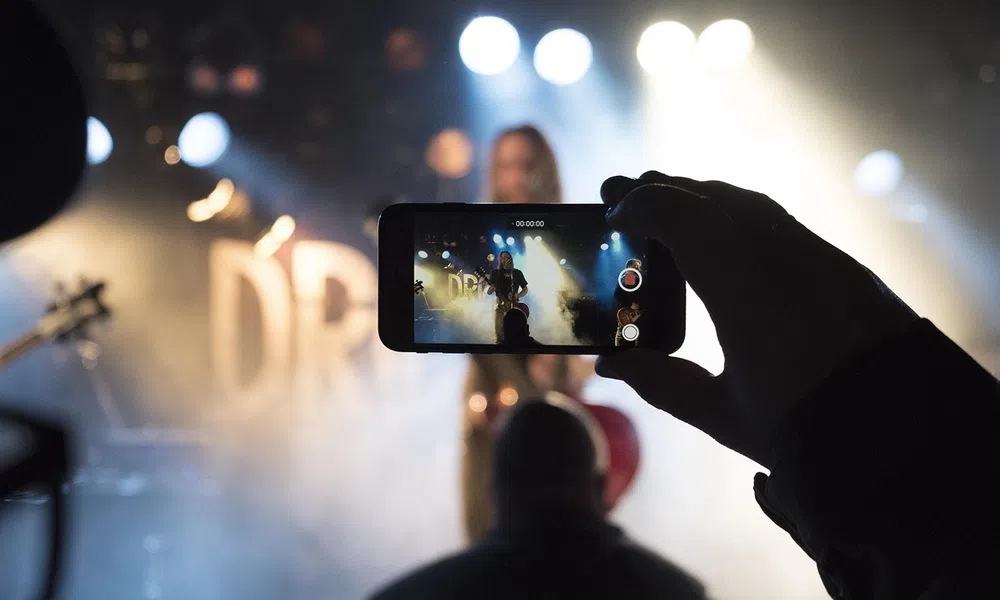 Person recording a live music performance on smartphone with stage lights and smoke effects in background