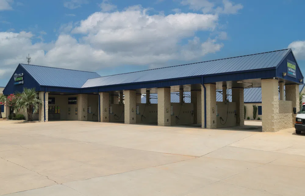 Self-service car wash facility with multiple bays and blue metal roofs under a partly cloudy sky.