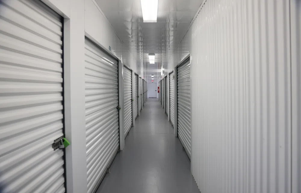 Long indoor hallway with rows of white storage unit doors on both sides under fluorescent lighting.