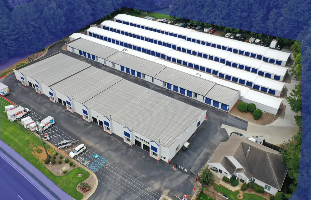 Aerial view of a self-storage facility with multiple white buildings and rows of storage units surrounded by greenery.