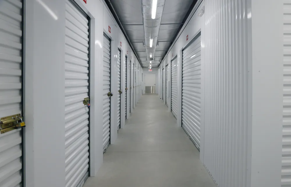 Indoor corridor with rows of white storage unit doors secured with locks in a self-storage facility.