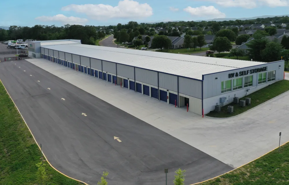 A large self-storage facility with multiple blue doors, surrounded by paved roads and nearby residential homes.