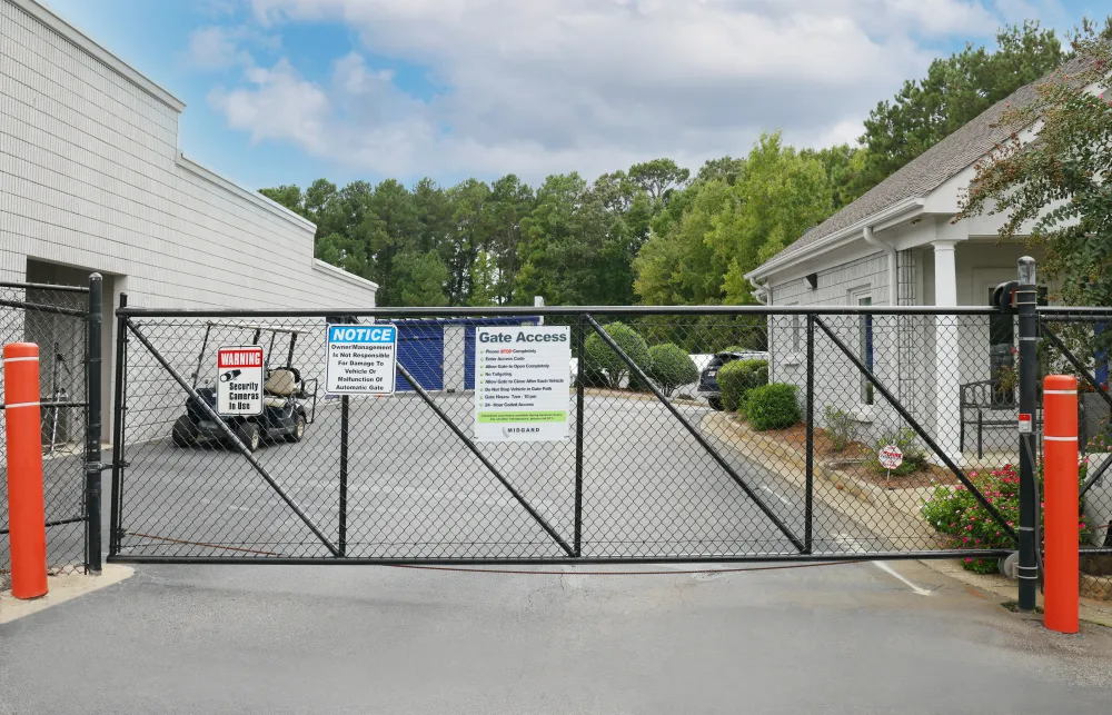 Black metal security gate with warning signs blocks entrance between two white buildings with greenery
