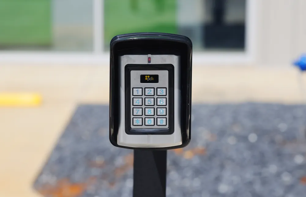 Black keypad access control device on a post with numbered buttons and PDK logo in outdoor setting.