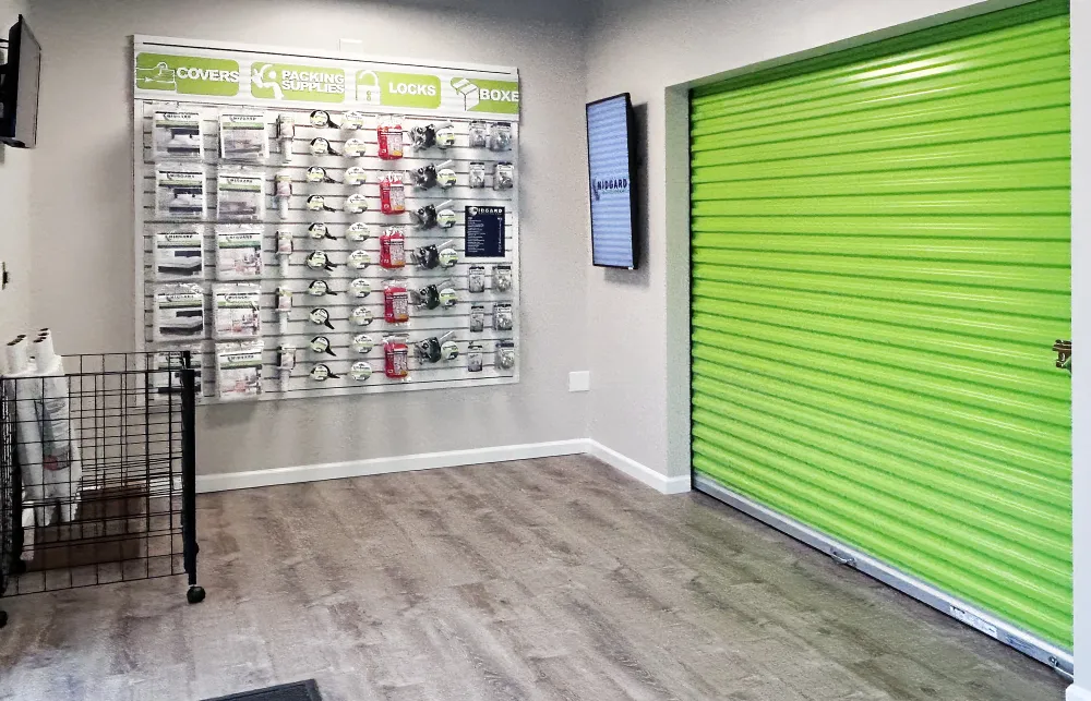 Interior of storage facility with green roll-up door and display wall of packing supplies and locks.