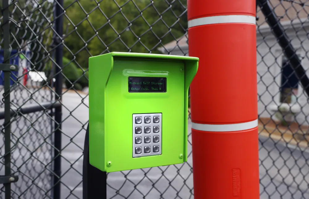 Bright green keypad access control box mounted next to a red column in an outdoor fenced area.