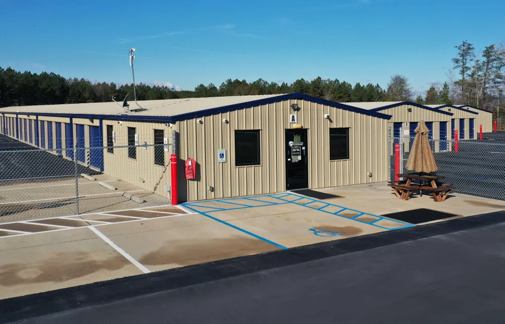 Storage facility with beige metal buildings, blue roll-up doors, fenced area, and a picnic table with umbrella