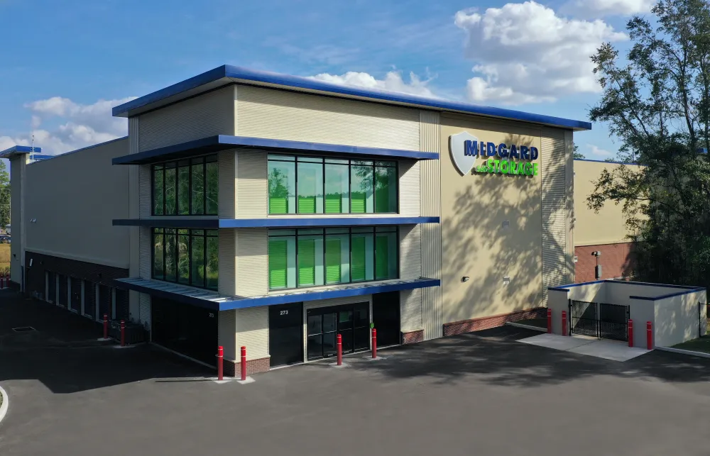 Modern Midgard Storage facility with green windows and secure gated parking under a blue sky.