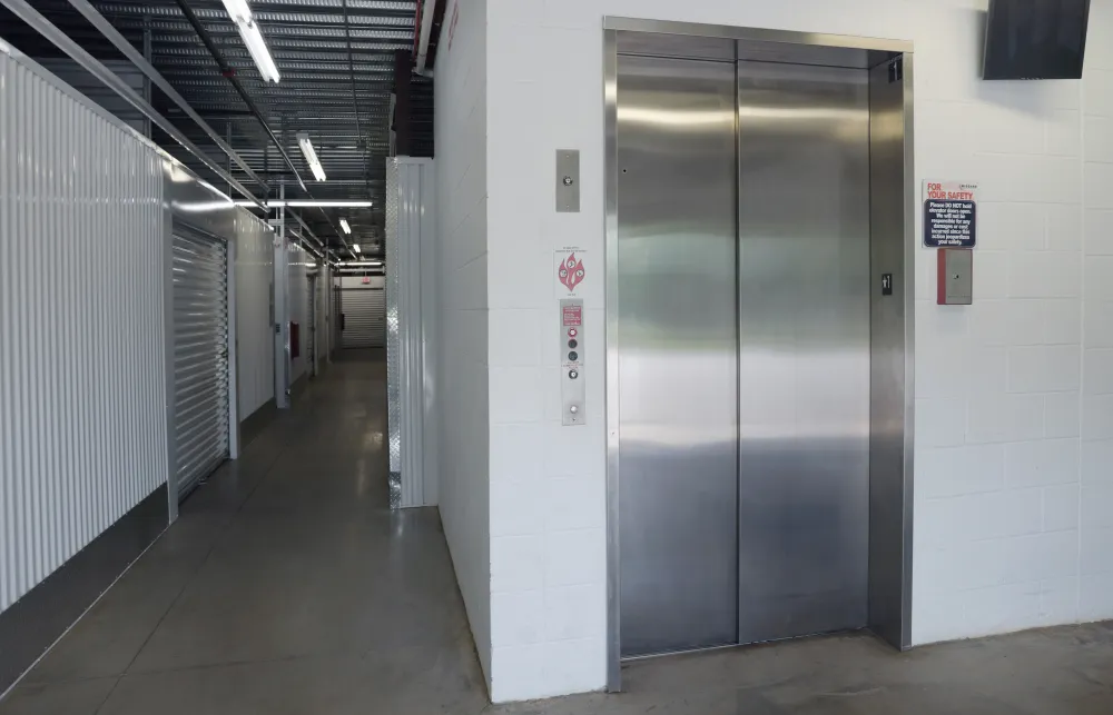 Stainless steel elevator in a clean storage facility hallway with metal roll-up doors and concrete floor.