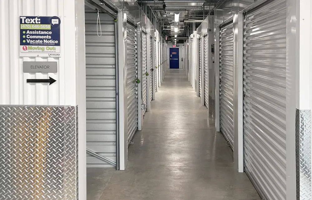 Indoor hallway of a self-storage facility with rows of closed, gray roll-up metal doors and concrete floor.