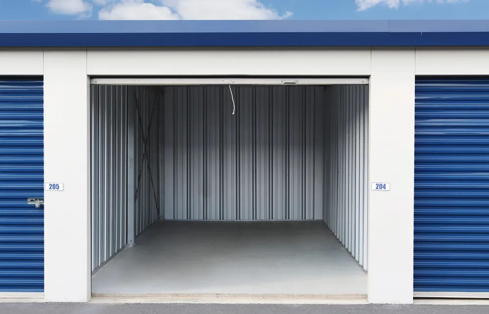 Empty storage unit 204 with open blue roll-up door in outdoor self-storage facility under blue sky.