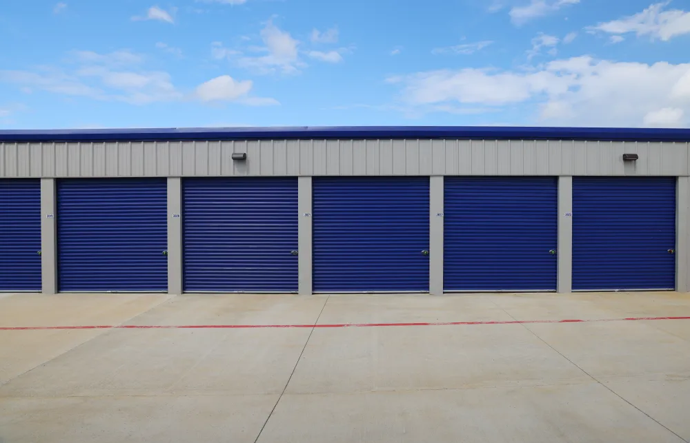 Row of blue storage unit doors with concrete driveway under a partly cloudy sky