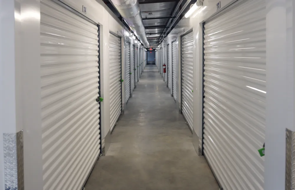 Long hallway of a modern storage facility with white metal roll-up doors and concrete floor