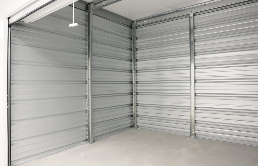 Empty indoor storage unit with gray metal walls and concrete floor, open roll-up door visible overhead.