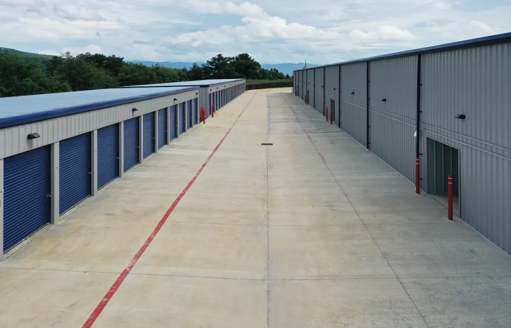 Outdoor storage facility with rows of blue roll-up doors and wide concrete driveway under cloudy sky.