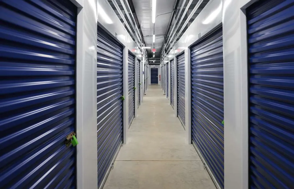 Interior view of a clean storage facility corridor with blue roll-up doors secured with locks.