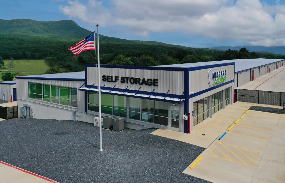 Modern self storage facility with American flag, parking, and mountainous landscape in background under blue sky.