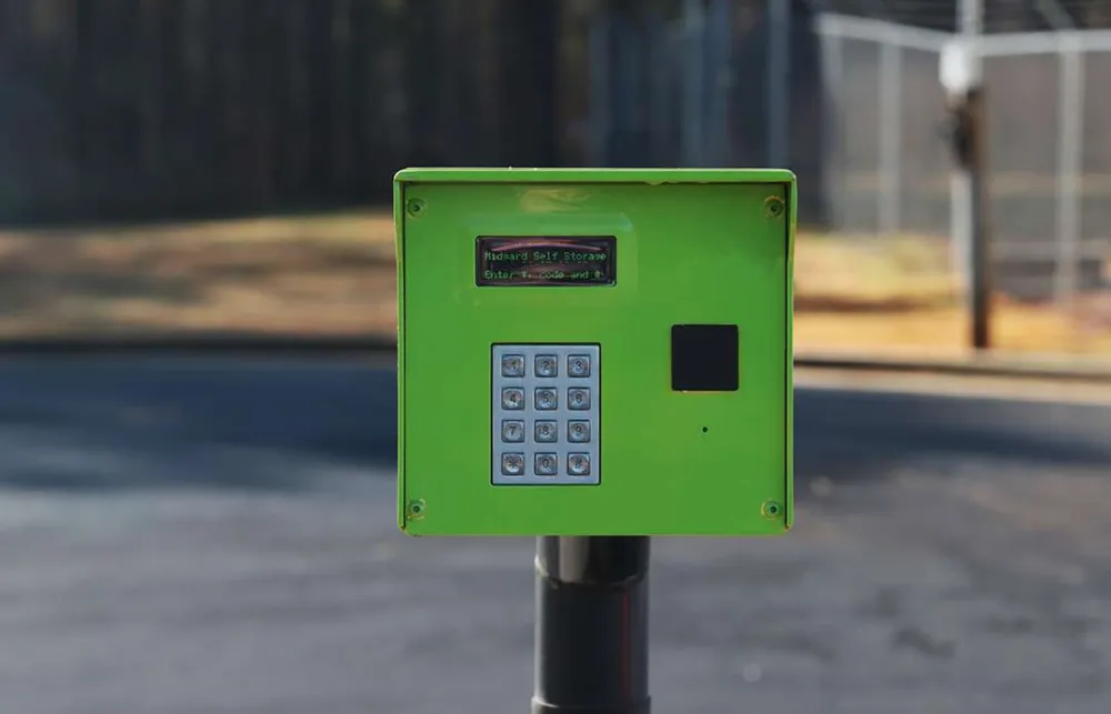 Green keypad access control panel for gated entry with numeric buttons and small display screen.