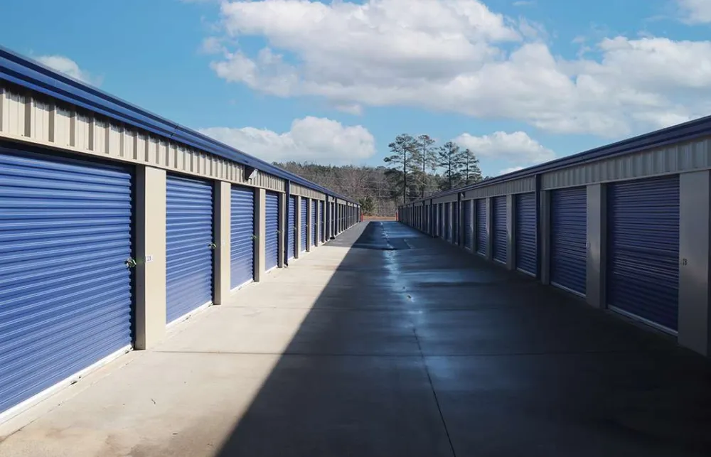 Outdoor self-storage units with blue rolling doors under a partly cloudy sky on a sunny day