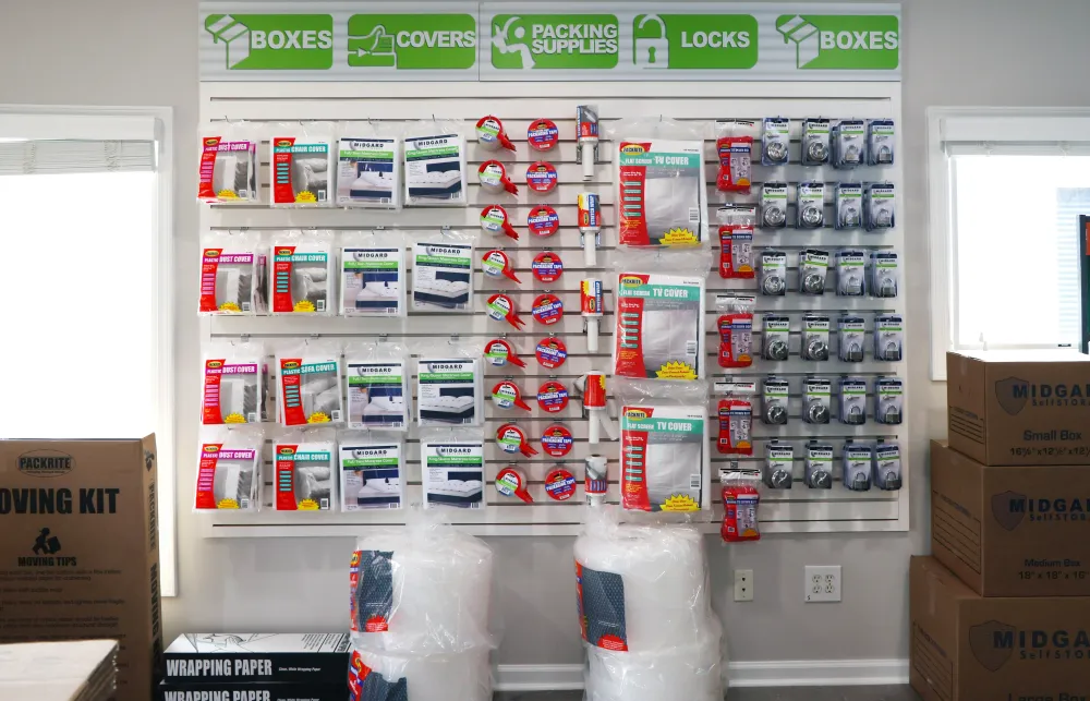 Wall display of moving and packing supplies including tape, covers, locks, and various boxes in a storage room.