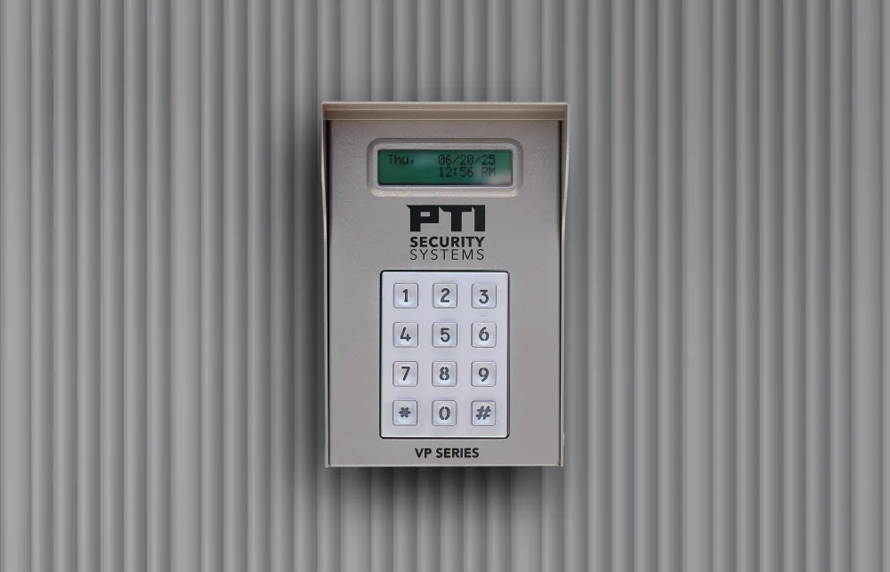 Digital security keypad mounted on a grey corrugated wall displaying date and time on screen.