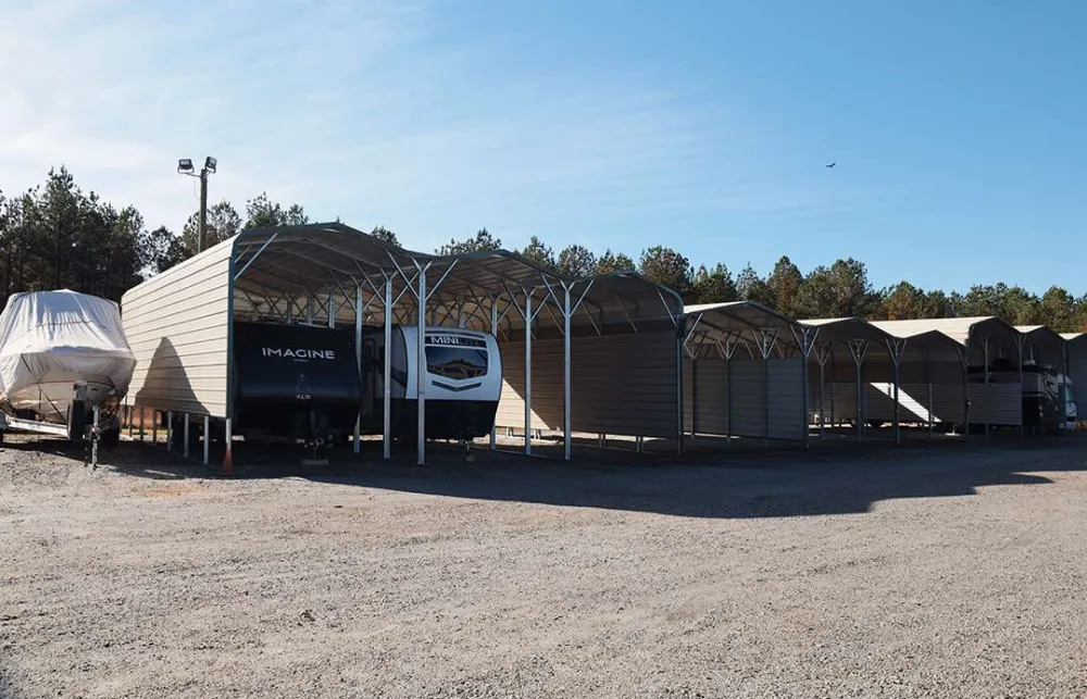 Outdoor storage units with metal roofs sheltering RVs and a covered boat under a clear blue sky.