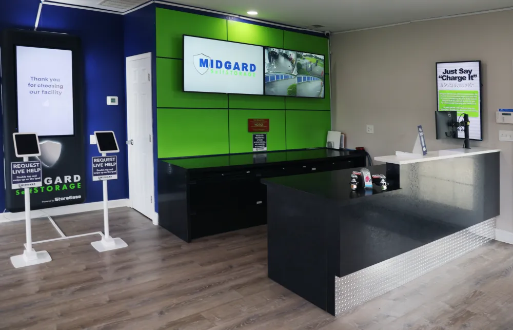 Modern storage facility lobby with black reception desk, green and blue wall panels, and digital signage
