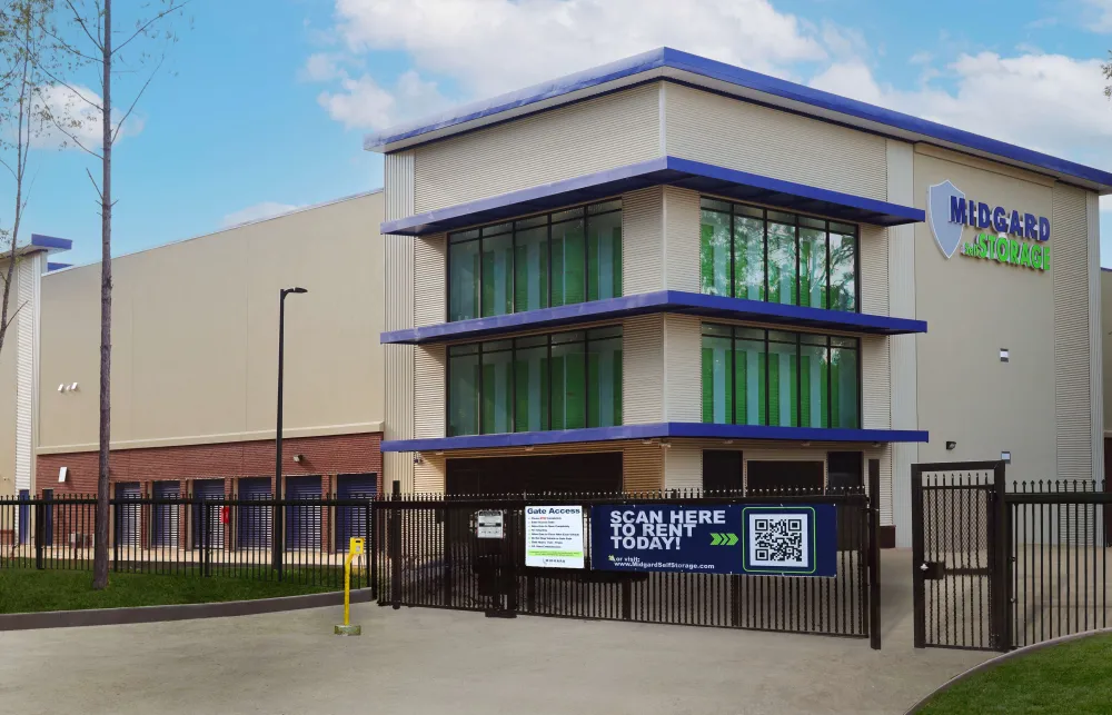 Modern self-storage facility with large windows, gated entrance, and outdoor signage under blue sky.