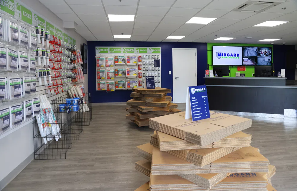 Interior of a self-storage store with packing supplies, stacked moving boxes, and a service counter with security monitors.