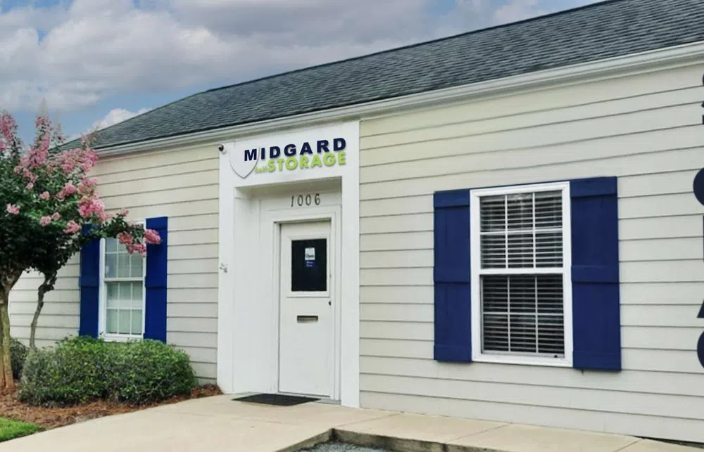 Midgard Storage building exterior with white siding, blue shutters, and a tree with pink flowers under a cloudy sky.