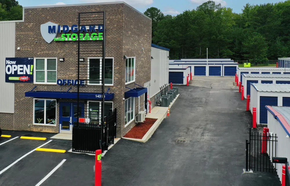 Midgard Storage facility with office building, storage units, and parking area amid greenery under blue sky.