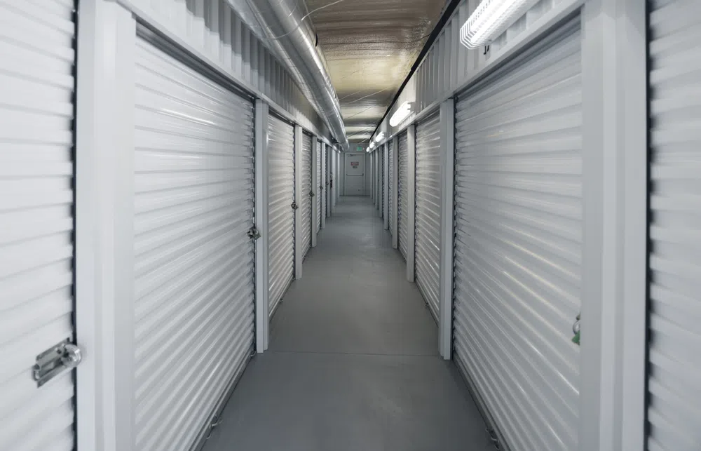 Long hallway with closed white metal storage unit doors in a clean, well-lit self-storage facility corridor.