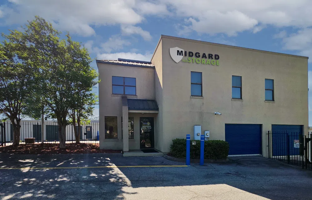 Midgard Storage building with beige walls, blue garage doors, and shaded trees under a partly cloudy sky.