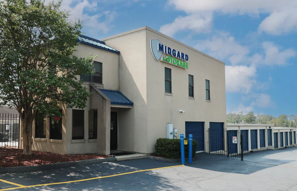 Midgard Self Storage facility with office building, storage units, tree, and blue sky on a sunny day.