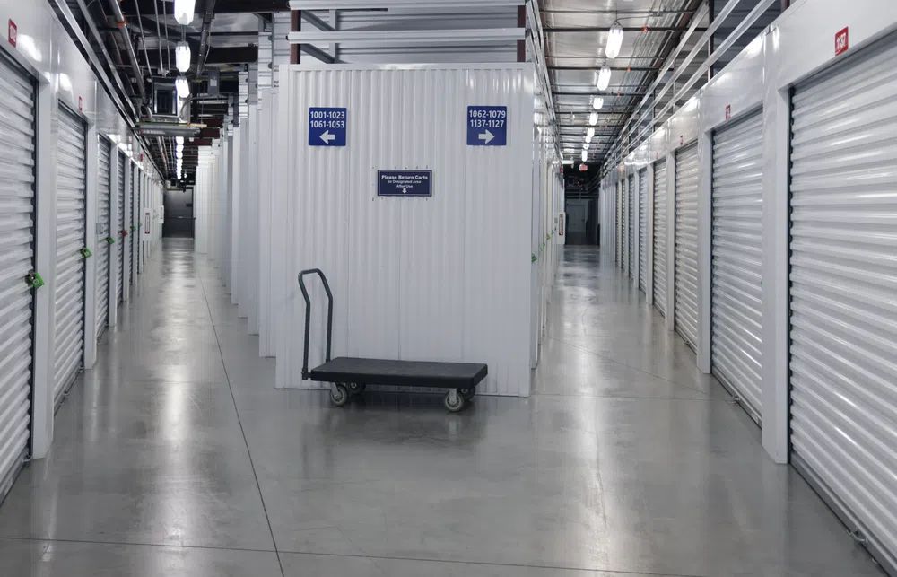 Empty indoor storage facility with closed white metal doors and a black flatbed cart in the center aisle.