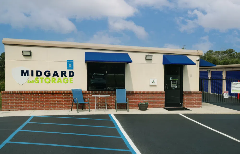 Midgard Self Storage facility office with blue awnings, chairs, table, and parking spots under a partly cloudy sky.