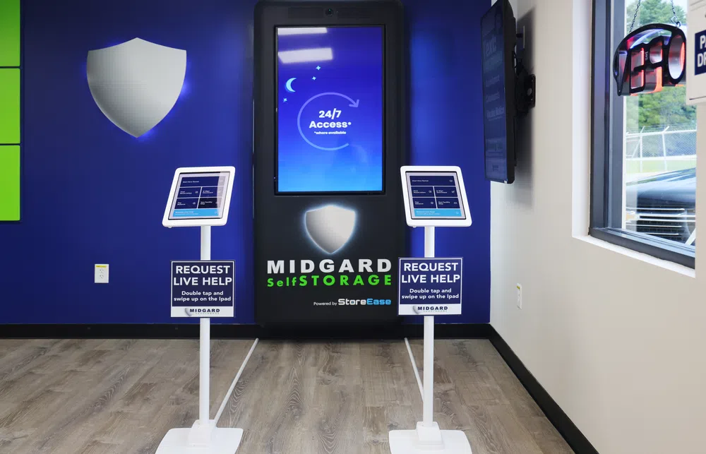 Midgard Self Storage kiosk with 24/7 access sign and two live help request iPads in a modern facility lobby.