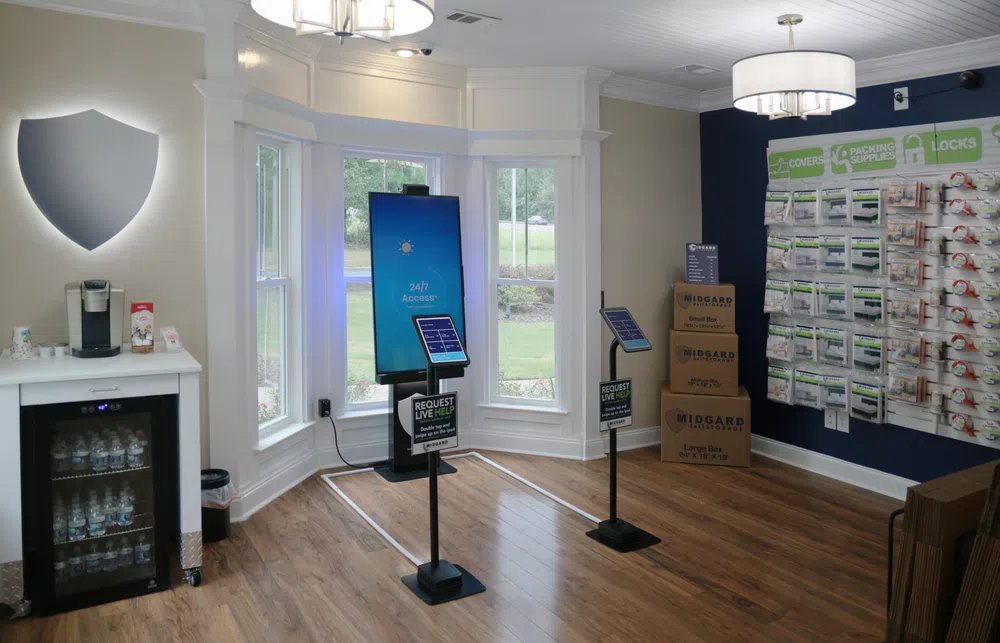 Modern self-service office with digital kiosks, packaged supplies, and water cooler in bright room with hardwood floor.