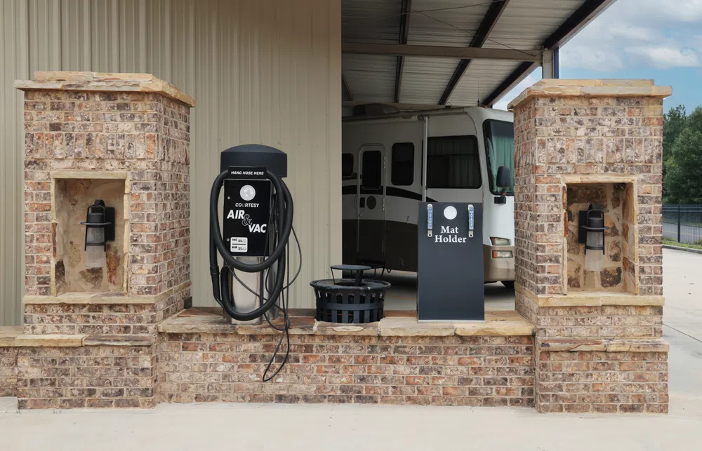Air and vacuum station with mat holder at RV park with brick pillars and parked motorhome in background.