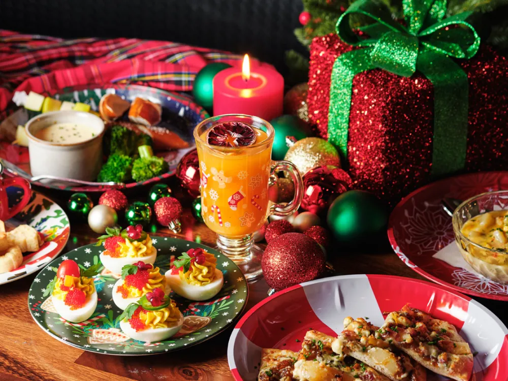 Festive Christmas table with deviled eggs, cocktail, pizza slices, gift box, and holiday decorations.