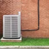 Outdoor air conditioning unit installed on a concrete slab next to a red brick wall with green grass below.