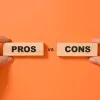Hands holding wooden blocks with PROS and CONS text against orange background to illustrate comparison.