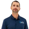 Man wearing navy polo shirt with PV logo, beige pants, brown belt, and brown shoes standing confidently.