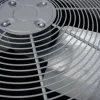 Close-up of a metal fan blade behind a protective circular grill in an air conditioning unit.