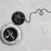 Close-up of a bathtub drain with a metal chain attached to a black rubber stopper on a wet surface.
