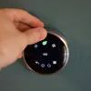 Hand adjusting a smart thermostat showing eco mode with green leaf icon on digital display.