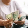 Close-up of a person counting US dollar bills while sitting at a table with a wallet and credit cards.