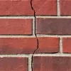 Close-up of a red brick wall with a vertical crack running through the mortar and bricks.