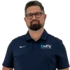Man wearing navy blue polo with PV logo, khaki pants, brown belt, brown shoes, and glasses standing with hands in pockets.